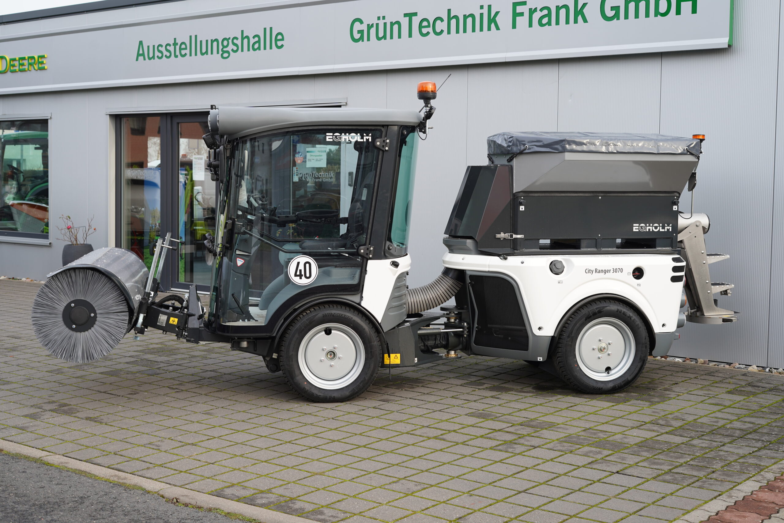 Weiße Erholm City Ranger Kehrmaschine mit Saugfunktion vor GrünTechnik Frank – Kommunale Reinigungstechnik