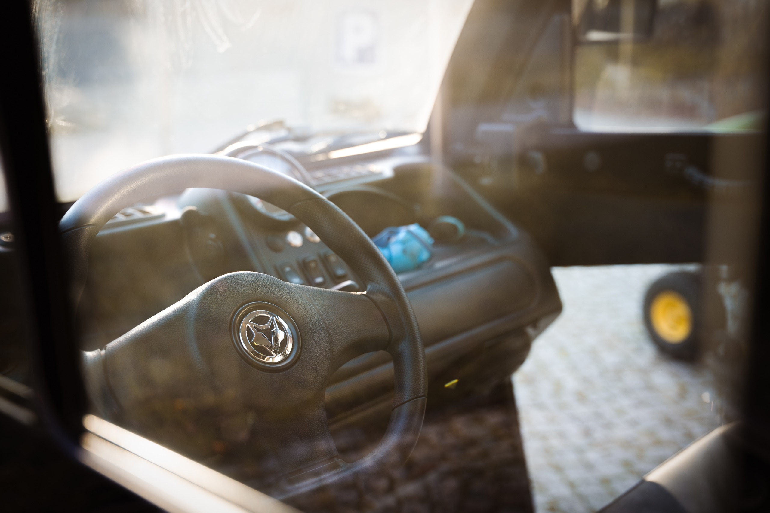 Nahaufnahme des Fahrerplatzes eines Goupil Elektro-Nutzfahrzeugs mit Fokus auf das Lenkrad und das Firmenlogo, fotografiert durch die Seitenscheibe.