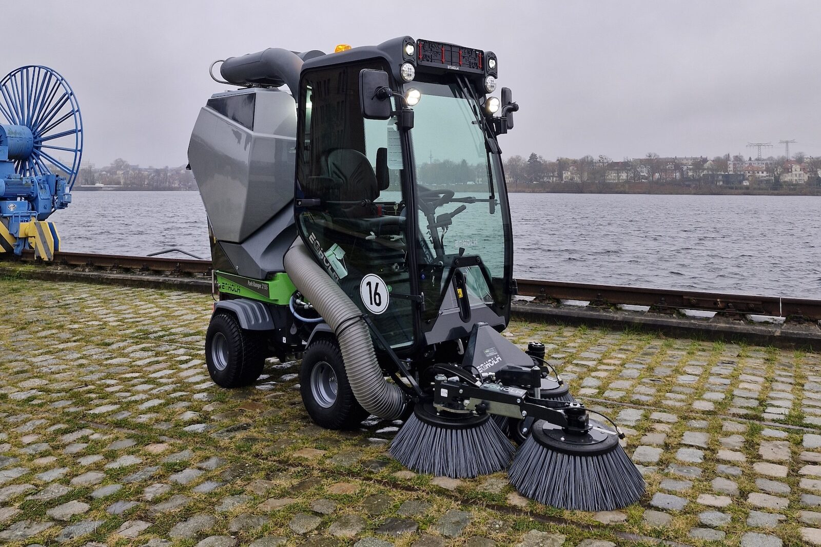 Grüne kompakte Kehrmaschine mit Saugfunktion bei Flächenreinigung am Wasser – GrünTechnik Frank